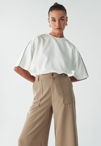 Top bianco a maniche corte con una vestibilità rilassata, caratterizzato da dettagli beige sulle spalle; abbinato a pantaloni beige a vita alta con gamba ampia.