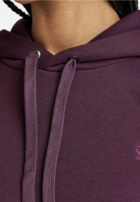 Close-up of person wearing a dark purple hoodie with thick drawstrings and braided hair visible at neck.