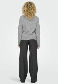 Siv sweatshirt z ohlapnim krojem, teksturirano tkanino in rebrastim robom, v kombinaciji z visoko pasom in širokimi temnimi hlačami z navpičnimi črtami.