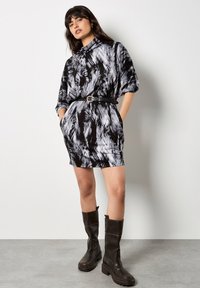 Czarna i biała wzorzysta krótka sukienka z kołnierzykiem, z paskiem w talii i bocznymi kieszeniami, w zestawie z wysokimi czarnymi botkami.