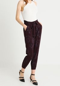 Pantalons à motif floral violet foncé avec une taille élastique et un lien, associés à un débardeur côtelé blanc et des escarpins noirs à bride à la cheville.