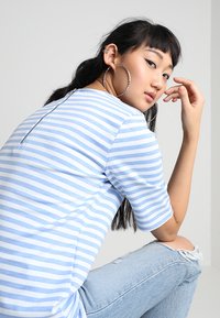 Blå og hvid stribet t-shirt med korte ærmer, der har en lynlåsdetaile på ryggen, parret med lyseblå ripped jeans.