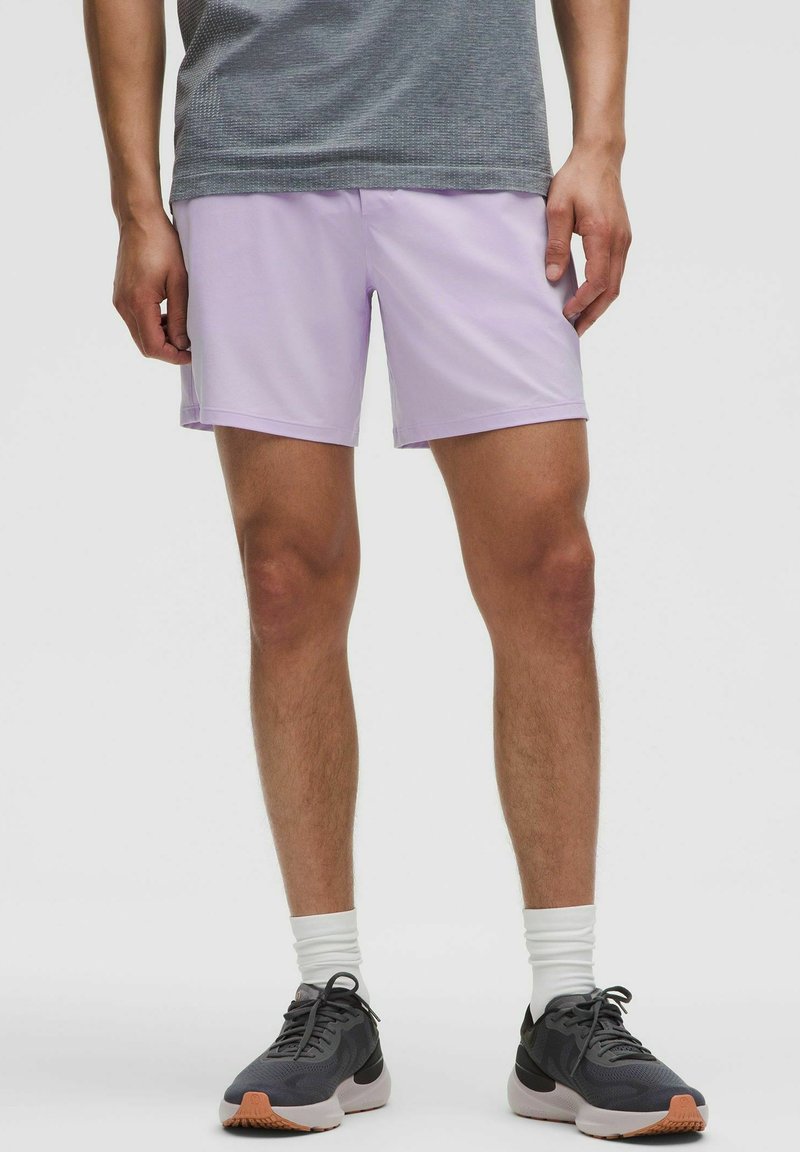 Shorts de sport violet clair avec une texture lisse, associés à un t-shirt à manches courtes gris à motifs et des chaussures de course noires.