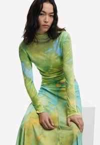 Top a maniche lunghe, aderente, di colore verde con motivi tie-dye blu e giallo, abbinato a una gonna maxi fluida, di colore teal, con dettagli delle cuciture sottili.