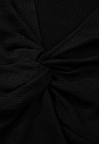 Tissu noir texturé torsadé en une spirale serrée, montrant des plis et un motif subtil ondulé en surface.