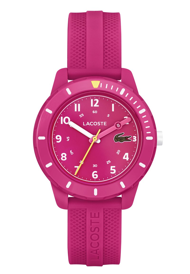 Montre en silicone rose avec un boîtier rond, aiguilles jaunes et blanches, marqueurs d'heure de 12 heures et logo de crocodile Lacoste sur le cadran. Bracelet texturé.