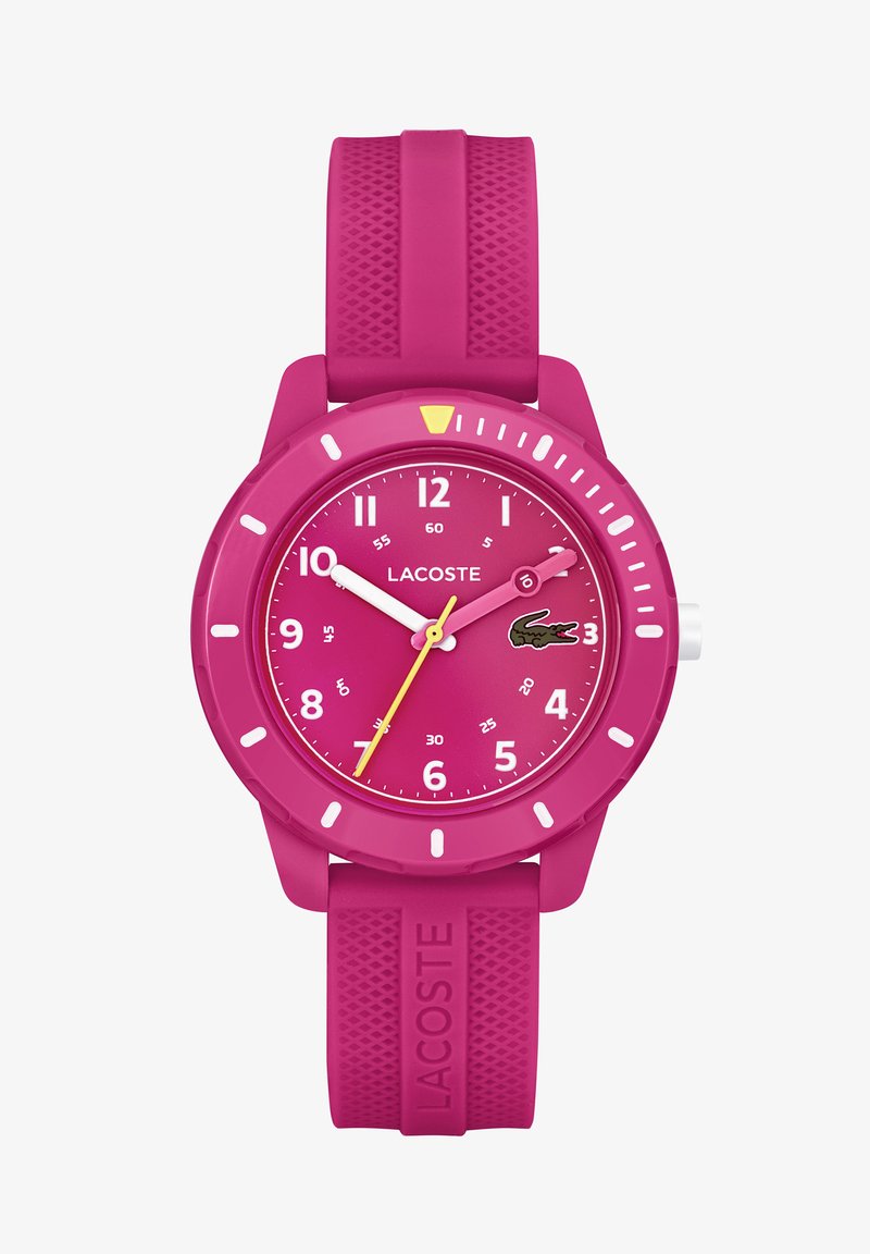 Reloj de silicona rosa con caja redonda, manecillas amarillas y blancas, marcadores de 12 horas y el logo del cocodrilo de Lacoste en la esfera. Correa texturizada.