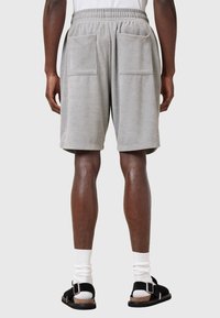 Grå fleece shorts med elastisk talje, der har to store baglommer. Båret med sorte sandaler og hvide sokker.