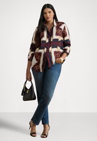 Πουκάμισο με κουμπιά μπροστά και πολύχρωμο γεωμετρικό σχέδιο σε αースΤόνους, συνδυασμένο με μπλε τζιν με ίσια πόδια και μαύρη τσάντα χειρός.