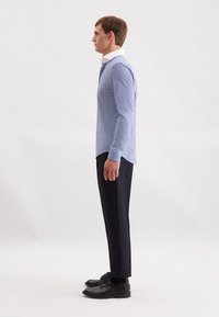 Camicia a righe blu e bianche con colletto a punta, abbinata a pantaloni neri e scarpe eleganti nere lucidate.
