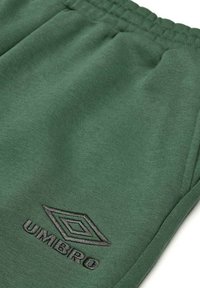 Jogging en coton vert avec une taille élastique, présentant un logo Umbro noir brodé sur le côté gauche. Texture lisse, design décontracté.