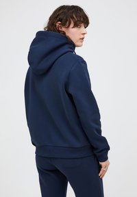 Felpa con cappuccio blu navy realizzata in tessuto morbido, caratterizzata da un orlo e polsini a coste, con una vestibilità rilassata e un design minimal.