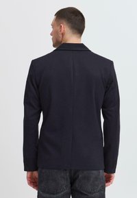 Blazer marine à texture lisse, fente unique au dos et trois boutons décoratifs sur les manches. Coupe ajustée.