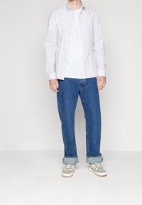 Pruhovaná košile s knoflíky v bílé a světle šedé barvě, přes obyčejné bílé tričko, spojená s modrými džíny a šedými teniskami.