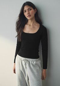 Zwarte geribbelde lange mouwen top met een vierkante halslijn, gecombineerd met lichtgrijze sweatpants met een elastische taille en trekkoord.