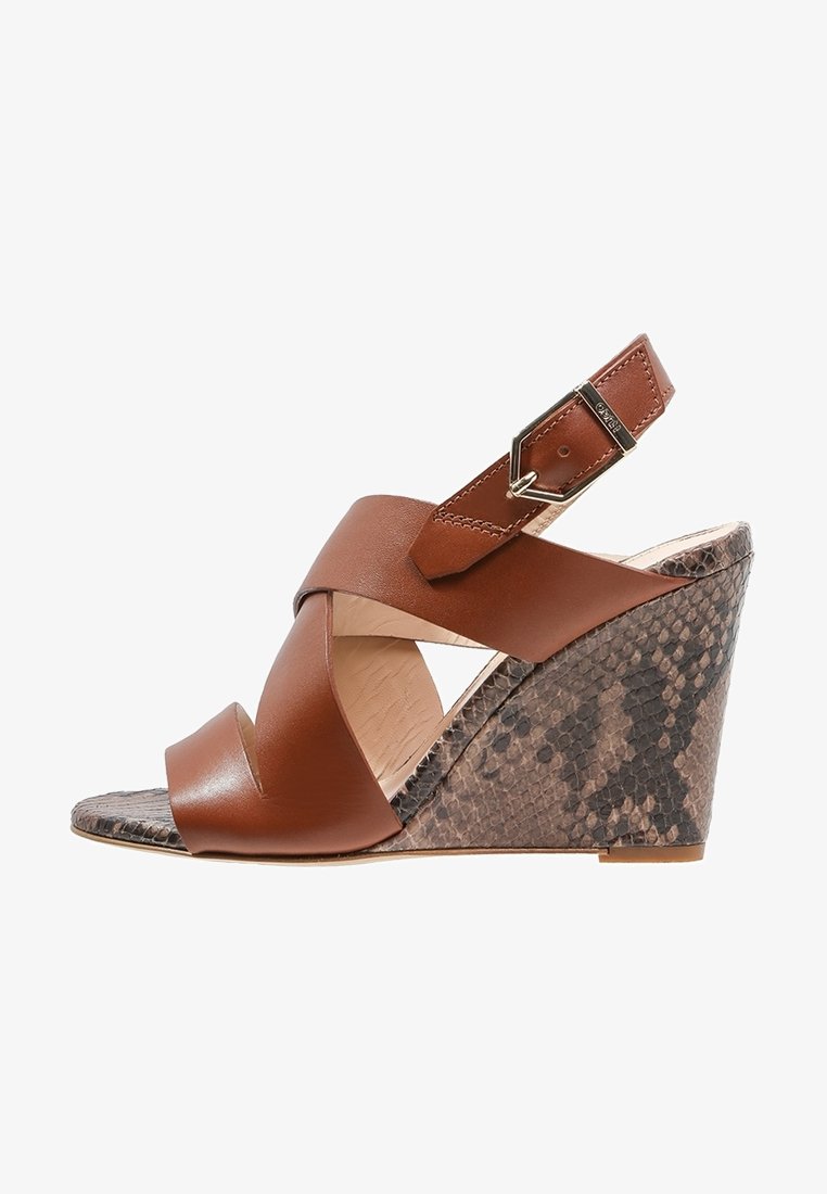 Sandale compensée en cuir marron avec un design de bride croisée, talon texturé en imprimé serpent et lanière de cheville réglable avec quincaillerie métallique.