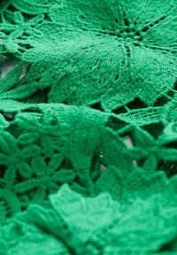 Tissu en dentelle verte brodée présentant des motifs floraux avec des motifs complexes, des textures variées et une finition douce et détaillée.
