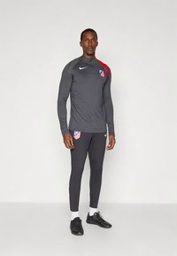 Survêtement de sport gris à manches longues, pantalon ajusté, accents rouges et logo de l'équipe sur la poitrine. Marque Nike affichée de manière proéminente.