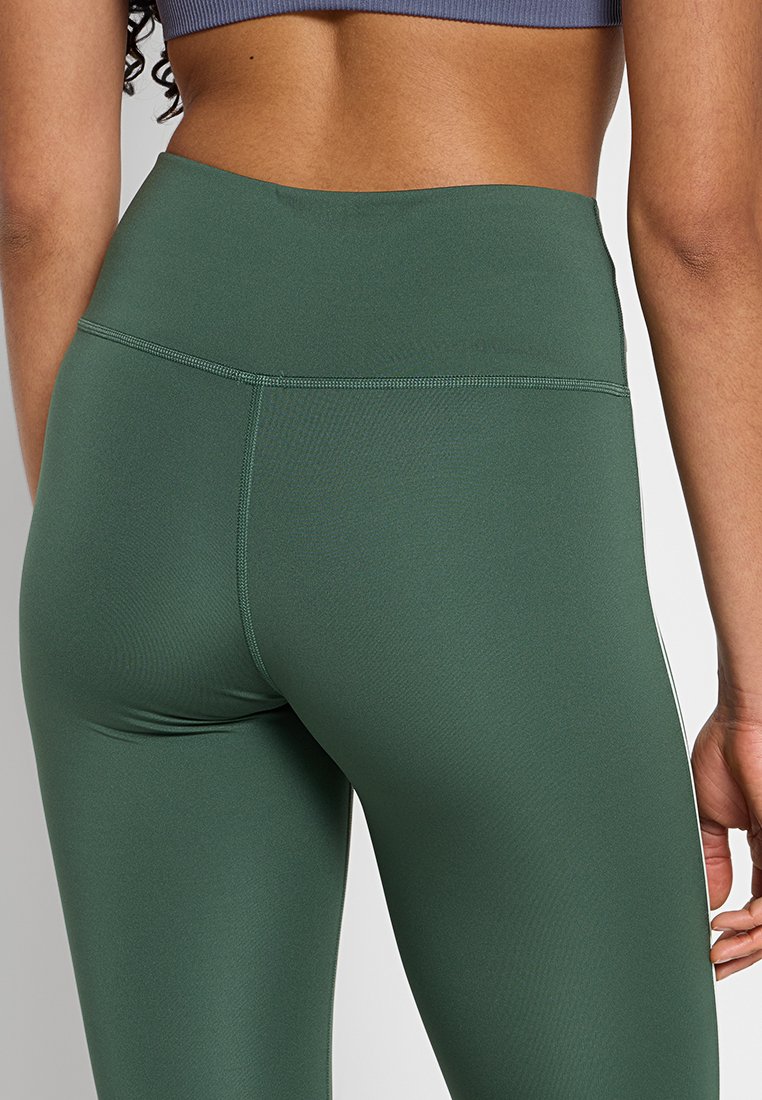 Leggings verdi a vita alta realizzati in tessuto elastico, con cuciture piatte e una superficie liscia. Vista della parte posteriore e della vita.
