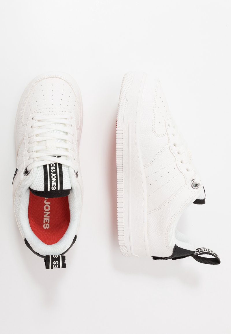 Baskets blanches avec un dessus en cuir texturé, des détails perforés, des languettes noires et blanches, et une doublure intérieure rouge.