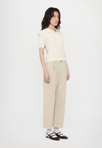 Knit, short-sleeve polo shirt in light beige with a placket and buttons; paired with loose-fitting, high-waisted beige trousers and black shoes.