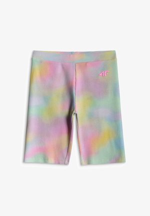 Dziecko ubrane w fioletową bluzę z kapturem i zamkiem błyskawicznym, beżowy krótki top, pastelowe krótkie spodnie rowerowe typu tie-dye, białe skarpetki i białe trampki, stoi z jedną zgiętą nogą.
