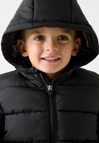 Schwarze Daunenjacke mit Kapuze, ausgestattet mit einem Reißverschluss vorne und einem gesteppte Design. Glatte Textur mit glänzender Oberfläche und einem dreieckigen Reißverschluss-Zug.