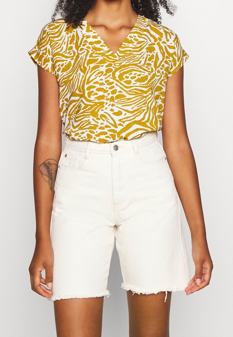 Top corto a maniche corte giallo e bianco con motivo a V, abbinato a pantaloni corti in denim bianco a vita alta con orlo sfilacciato.