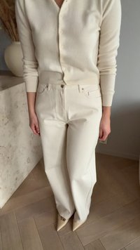 Smetanový svetr na knoflíky a béžové široké džíny s vysokým pasem, které mají přední kapsy a zapínání na knoflíky, doplněné světle zbarvenými špičatými botami.