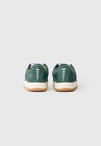 Pantofi sport verzi din suede, cu accente albe, spate texturat și tălpi din cauciuc de tip gumă, având detalii cu logo și orificii de ventilație pe laturi.