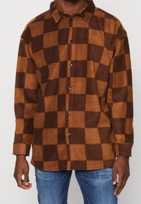 Chemise en flanelle à carreaux marron et beige avec col, fermeture à boutons et manches longues. Texture douce avec une coupe décontractée.