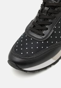 Sneaker nera con tomaia in tessuto testurizzato decorata con piccoli chiodi d'argento, lacci neri spessi e suola bianca e grigia.