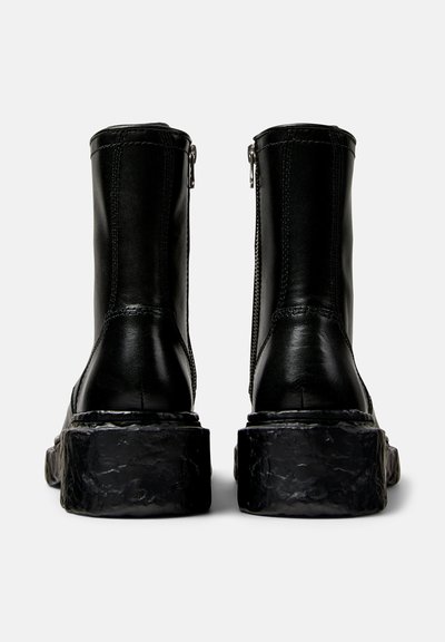Black leather ankle boots with a chunky black textured sole, featuring side zippers and stitched detailing on the shaft.