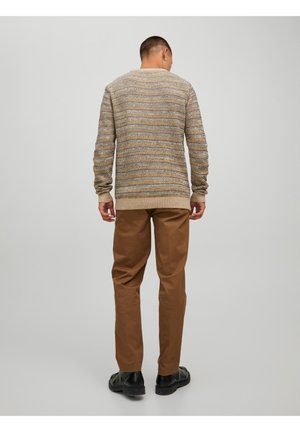 Beige gestrickter Pullover mit mehrfarbigen horizontalen Streifen, kombiniert mit braunen Hosen und schwarzen Schuhen. Fokus auf Textur und Design.