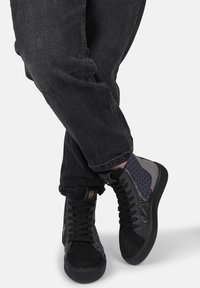 Sneakers alte con tomaia in suede e pelle nera, dettagli laterali grigi, motivo texturizzato e suola in gomma. Visibili lacci e dettagli del marchio.