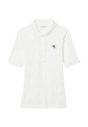 Polo bianco con maniche corte, tessuto testurizzato, cinque bottoni e una tasca frontale con un piccolo dettaglio del logo verde Lacoste.
