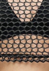 Μαύρο διχτυωτό ύφασμα με μεταλλικές κλωστές καλύπτει γυμνό δέρμα και μαύρο ένδυμα από κάτω, σχηματίζοντας σχέδιο κυψελώματος.