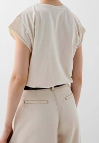 Top beige a maniche corte realizzato in tessuto morbido, con vestibilità ampia e orlo arrotondato, abbinato a pantaloni beige chiaro dotati di tasche posteriori.