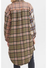 Ruudullinen flanellipaita vihreän, ruskean ja sinisen sävyissä, hieman kaartuvalla helmalla, napillinen kauluksella ja pitkillä hihoilla sekä vaihtelevilla ruutukuvioilla.