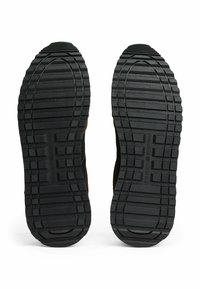 Suelas de zapatos de goma negra con un patrón de relieve texturizado que presenta ranuras horizontales y verticales para mayor tracción. Sin marcas visibles.