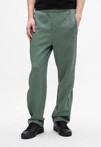 Hellgrüne Jogginghose mit strukturiertem Rautenmuster, elastischem Bund, Seitentaschen und getragen mit schwarzen Sneakers.