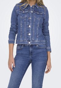 Blue denim jacket with a fitted design, featuring metallic buttons, two front pockets, and decorative embellishments on the fabric.