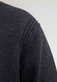 Dunkelblauer gestrickter Pullover mit einer glatten Textur und subtilen Rippdetails entlang der Schulternaht. Nahaufnahme hebt das Material hervor.