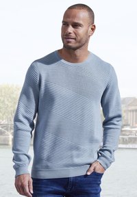 Hellblauer strukturierter Pullover mit rundem Ausschnitt, der horizontal und diagonal gerippte Muster aufweist, kombiniert mit dunkelblauen Jeans.