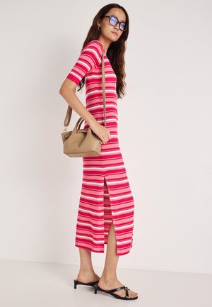 Rochie cu dungi roșii și roz, din material reiat, cu mâneci scurte și o crăpătură laterală. Asortată cu papuci negri și o poșetă mică bej.