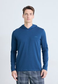 Langermet navy hettegenser laget av mykt stoff, med V-hals, en subtil logo på venstre side, og kombinert med rutete pysjbukser.