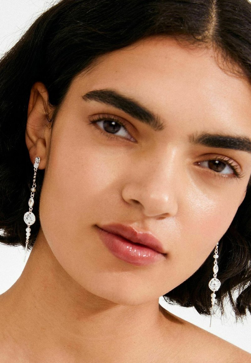 Silberne Tropfenohrringe mit runden und ovalen Perlen, klaren Kristallen und einem Perlakzent in einem langen, spitzen Design.