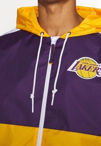 Lilla og gul vindjakke hoodie med lynlås foran, snoretræk og et trykt Los Angeles Lakers-logo på brystet.