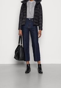 Czarna puchowa kurtka, biały top w wzory, ciemnoniebieskie dżinsy o szerokich nogawkach, czarne botki za kostkę i czarna torba. Gładkie tekstury i zorganizowany design.