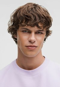 Sweatshirt crewneck violet clair avec un col côtelé. Le modèle a les cheveux bruns ondulés courts et un teint neutre, regardant directement l'objectif.